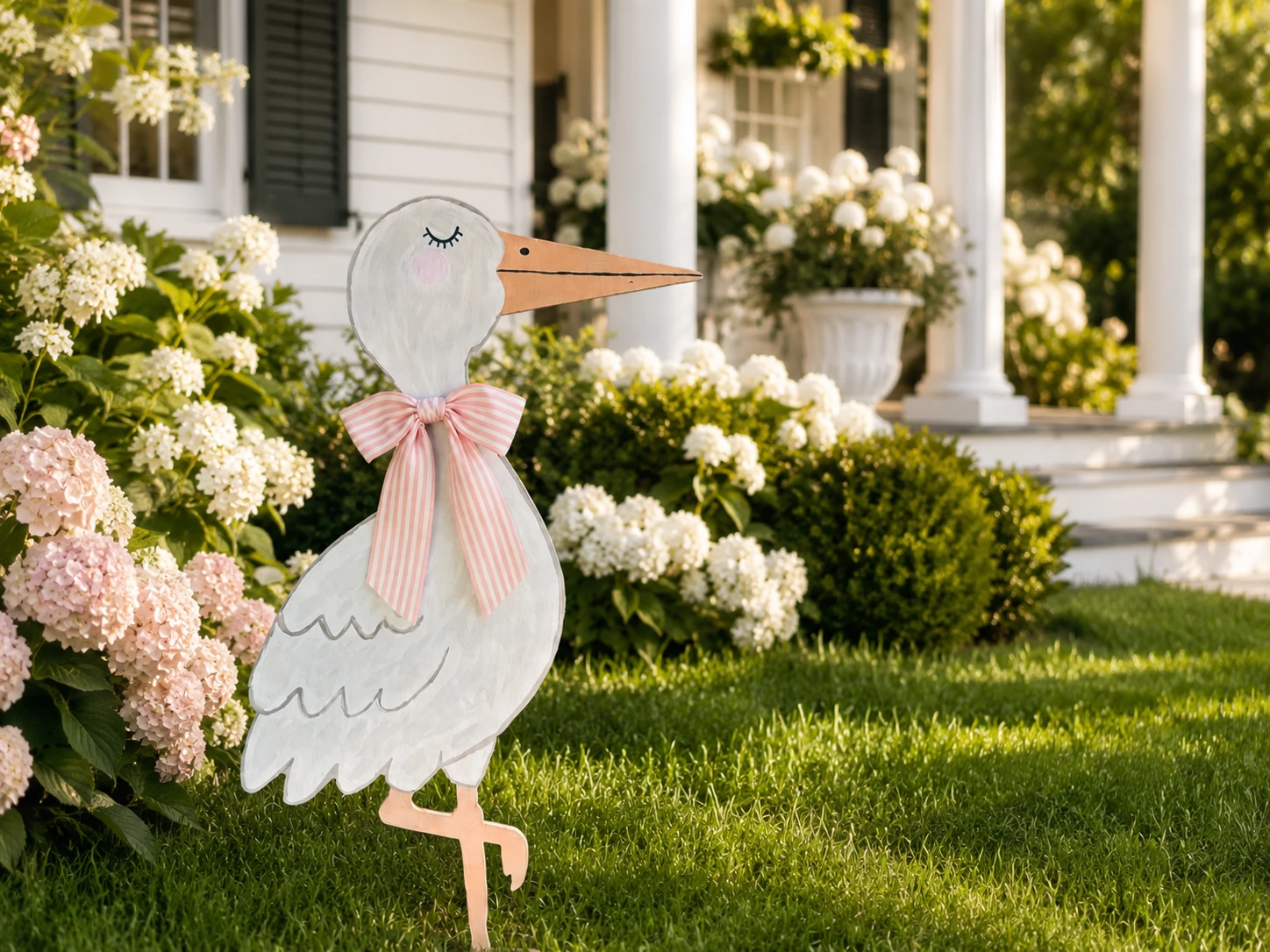 Pink bow stork yard display in front of a white home with hydrangeas